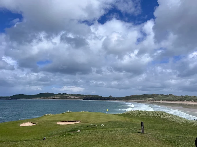 Par 3 finishing hole at Durness Golf Club with cliffs, ocean inlet, and sunset sky.